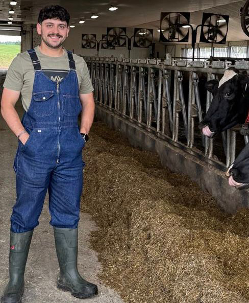 Jad Zinker standing in barn with dairy cows in back